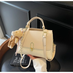 Detail der beigen Handtasche mit Webstruktur, goldenem U-Schloss und Bärenanhänger