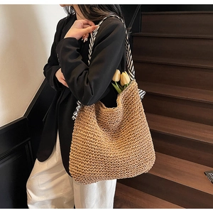 Straw tote bag with black and white striped scarf handle on a wooden staircase