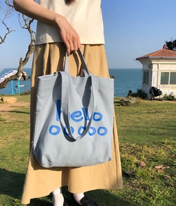 Detail van een blauwe canvas draagtas met hello ooooo tekst op een gazon aan de kust