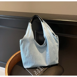 Dettaglio borsa tote in denim azzurro con manici neri a contrasto su una panca nera