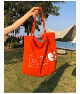 Détail d'un grand sac cabas en toile orange avec lettrage blanc sur fond de plage d'été