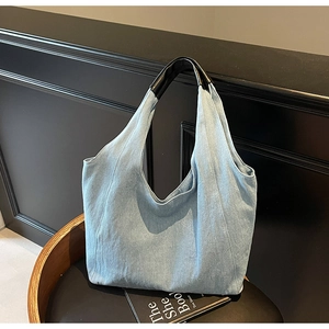 Dettaglio della borsa tote in denim azzurro con manici neri lucidi su una sedia di legno