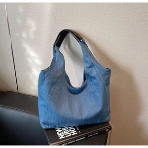Dettaglio della borsa hobo in denim blu con manici in pelle nera su sfondo minimalista