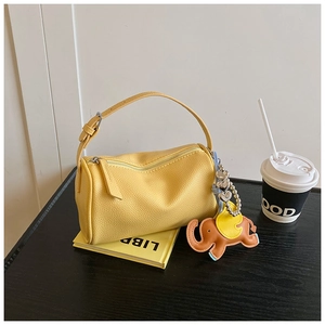 Detail of ginger yellow pebble leather barrel bag with elephant charm on dark wood table