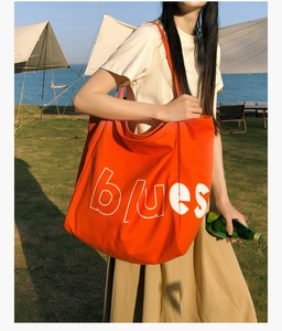 Vue détaillée d'un sac cabas en toile orange avec texte blanc sur fond de plage