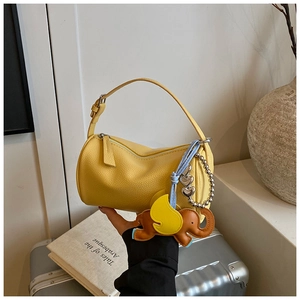 Detail of yellow lychee leather barrel bag with elephant charm and heart chain accessory