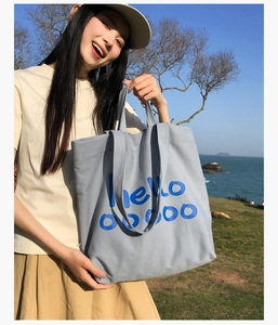 Detail van een lichtgrijze canvas tote bag met een blauwe hello-print in een buitenomgeving
