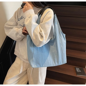 Dettaglio borsa tote in denim azzurro con manici in pelle nera su una modella donna