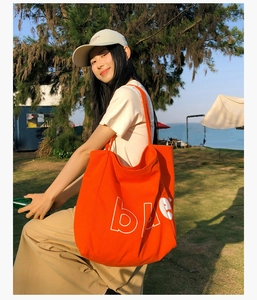 Photo en extérieur du grand sac cabas en toile orange avec texte bleu sur l'herbe