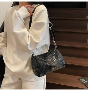 Detail of black woven cylinder crossbody bag with silver chain strap and metal logo plate