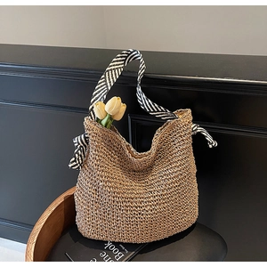 Detail of hand-woven straw tote with black and white striped handles on a dark seat