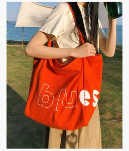 Détail d'un grand sac cabas en toile orange avec lettrage blues blanc sur l'herbe
