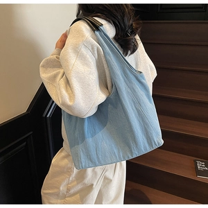 Dettaglio della borsa tote in denim azzurro con manici in pelle nera indossata da una modella