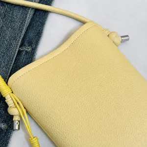 Detail of yellow pebbled leather crossbody bag with knot strap and silver hardware accents