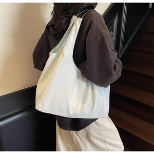 Dettaglio di una grande borsa hobo bianca con tracolle in pelle nera indossata sulla spalla
