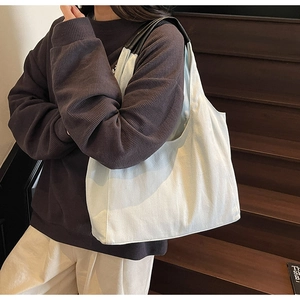 Dettaglio della borsa tote in tela bianca con manici in pelle nera indossata da una modella