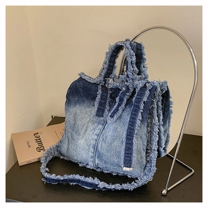 Détail du sac cabas en denim bleu dégradé avec bords effilochés et bandoulière amovible