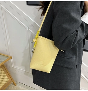 Dettaglio borsa a secchiello giallo con logo SUNWOMEN e tracolla intrecciata su cappotto