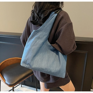 Dettaglio della grande borsa tote in denim blu indossata a spalla con trama del tessuto
