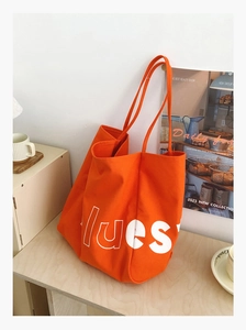 Grand sac cabas en toile orange avec lettrage lues blanc sur un bureau en bois