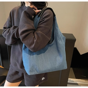 Grande borsa tote in denim blu con manici in pelle nera indossata sulla spalla