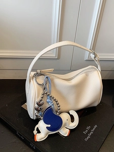 White lychee leather cylinder handbag with elephant charm on a decorative art book