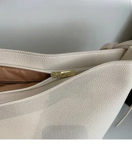 Gros plan sur la fermeture éclair dorée et le cuir grainé du sac à main de couleur crème