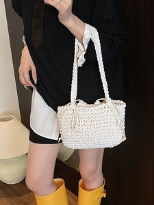 White woven bucket bag with braided straps and tassels shown on a model in a modern room