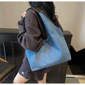 Dettaglio della borsa tote in denim blu con cinturini in pelle indossata da una modella