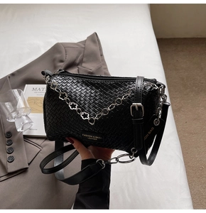 Detail of black woven texture handbag with silver floral chain and adjustable shoulder strap