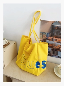 Détail d'un sac fourre-tout en toile jaune avec lettrage bleu sur une table en bois chic