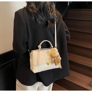 Detail der eleganten beige Umhängetasche mit strukturiertem Leder und Bärenanhänger