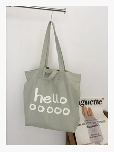 Detailopname van lichtgroene canvas draagtas met hello-print hangend aan een rek