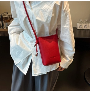 Dettaglio mini borsa a secchiello in pelle rossa con pendente in metallo e nodo sulla tracolla