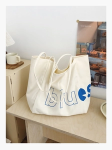 Détail du grand sac cabas en toile montrant le lettrage bleu vif sur un tissu blanc cassé