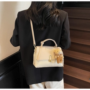 Detail der cremefarbenen Umhängetasche mit Flechtboden, Metallschloss und Bären-Anhänger