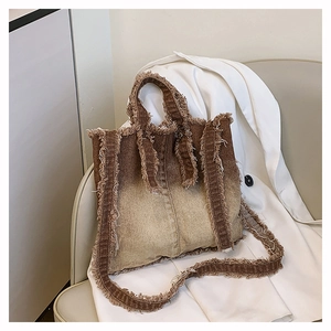 Détail d'un sac cabas en denim dégradé avec bords effilochés sur fond de costume blanc