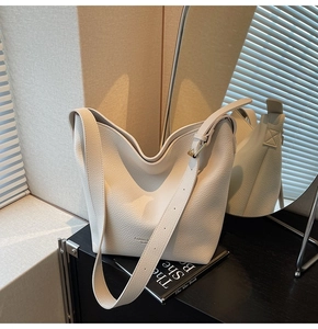 Gros plan d'un sac seau en cuir crème avec boucle dorée sur un meuble noir moderne