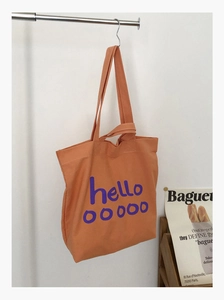 Detail van een oranje canvas draagtas met hello-opdruk aan een metalen standaard