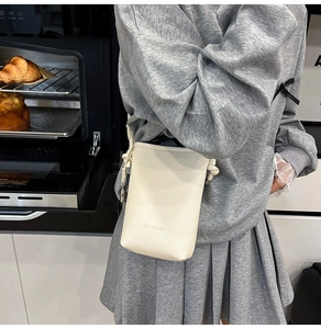 Dettaglio della borsa a tracolla in pelle bianco sporco con texture a grana e logo