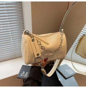 Close-up of cream woven cylindrical crossbody bag with floral chain and fashion charm