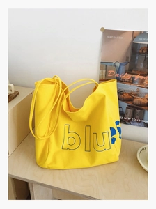 Vue détaillée d'un sac cabas en toile jaune avec lettrage bleu sur une table rustique