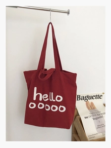 Detailweergave van de rode canvas tote bag met witte hello-print aan een metalen rek