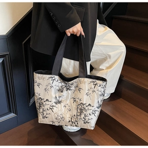 Detail of large tote bag featuring ink bamboo print and black handles held by model