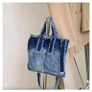 Détail des bords effilochés et dégradé bleu-blanc sur le sac cabas en jean suspendu