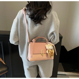 Rosa Lederhandtasche mit gewebter Bodenstruktur, Goldschloss und braunem Bärenanhänger am Riemen