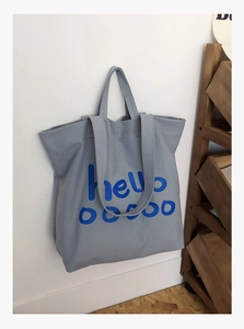 Detail van grijze canvas shopper met blauwe hello ooooo print op witte wand