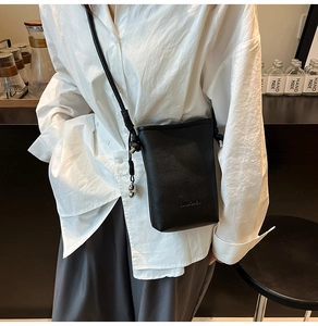 Dettaglio borsa a secchiello nera grana litchi con tracolla sottile e charm in metallo