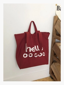 Detail van rode canvas draagtas met witte hello-opdruk en brede comfortabele schouderbanden