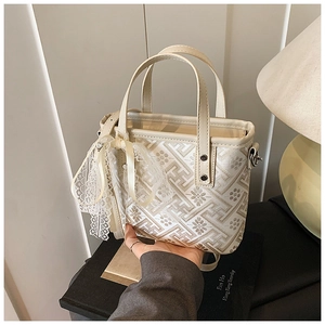 Close-up of white leather bucket bag featuring geometric flower print and lace bow detail